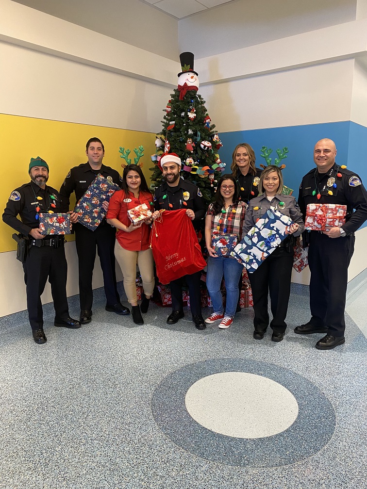 Police Officers and other participants holding presents in front of a Christmas tree